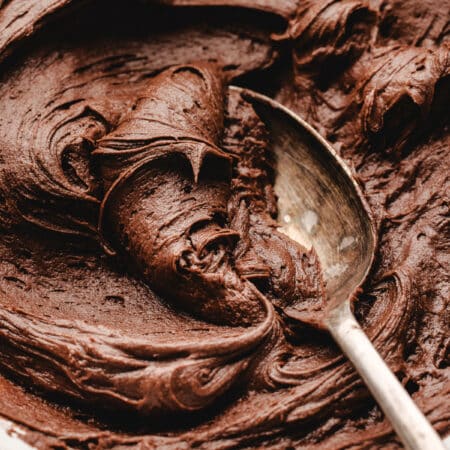 A silver spoon in a bowl of chocolate buttercream frosting.