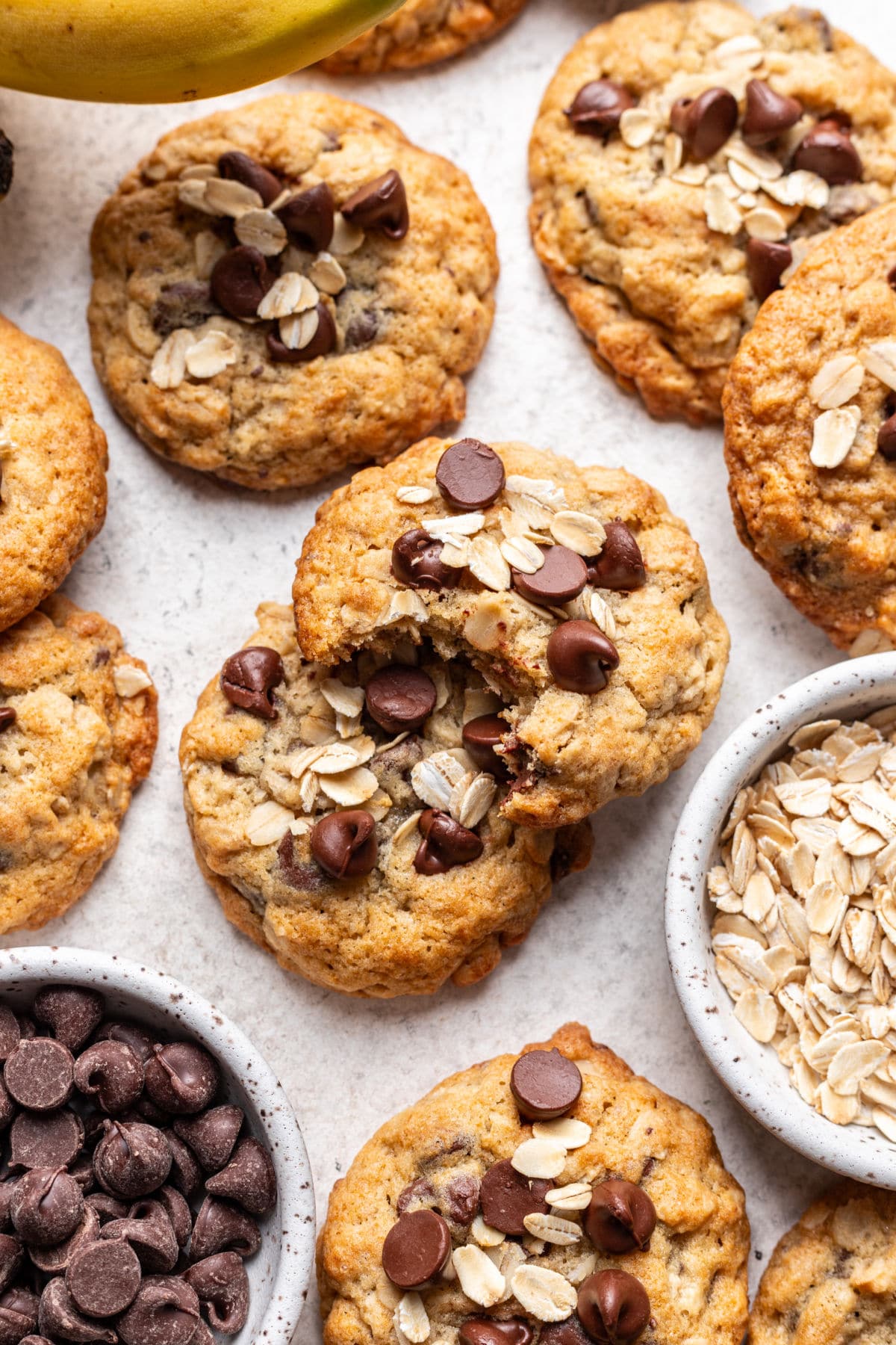 An oatmeal banana chocolate chip cookie with a bite missing on top of more cookies.