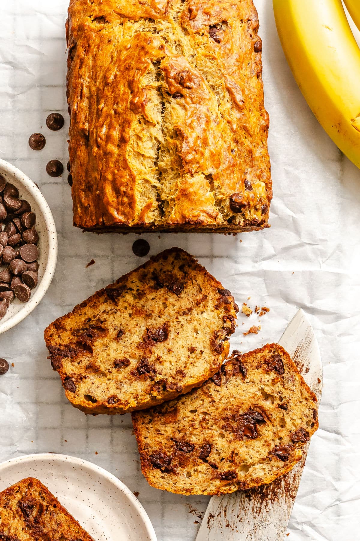 Two slices of chocolate chip banana bread next to the loaf. 