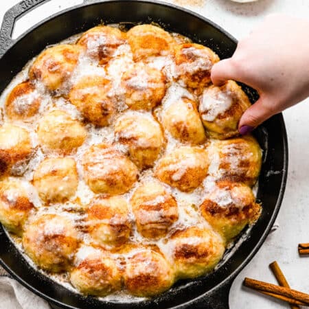 A hand pulling up a piece of cinnamon roll bites from a skillet.