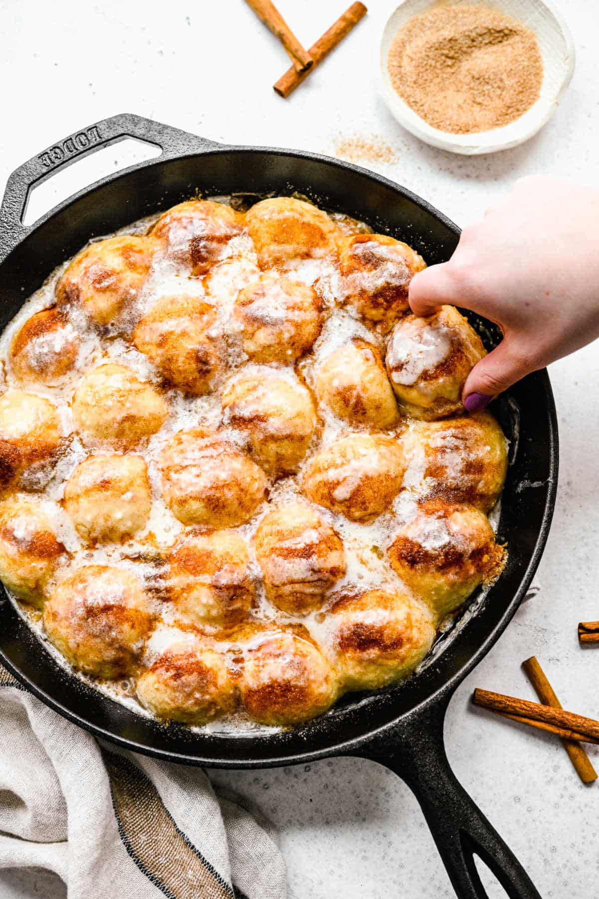 A hand pulling up a piece of cinnamon roll bites from a skillet.