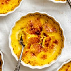 A ramekin of creme brulee with a spoon in it surrounded by more ramekins of creme brulee.