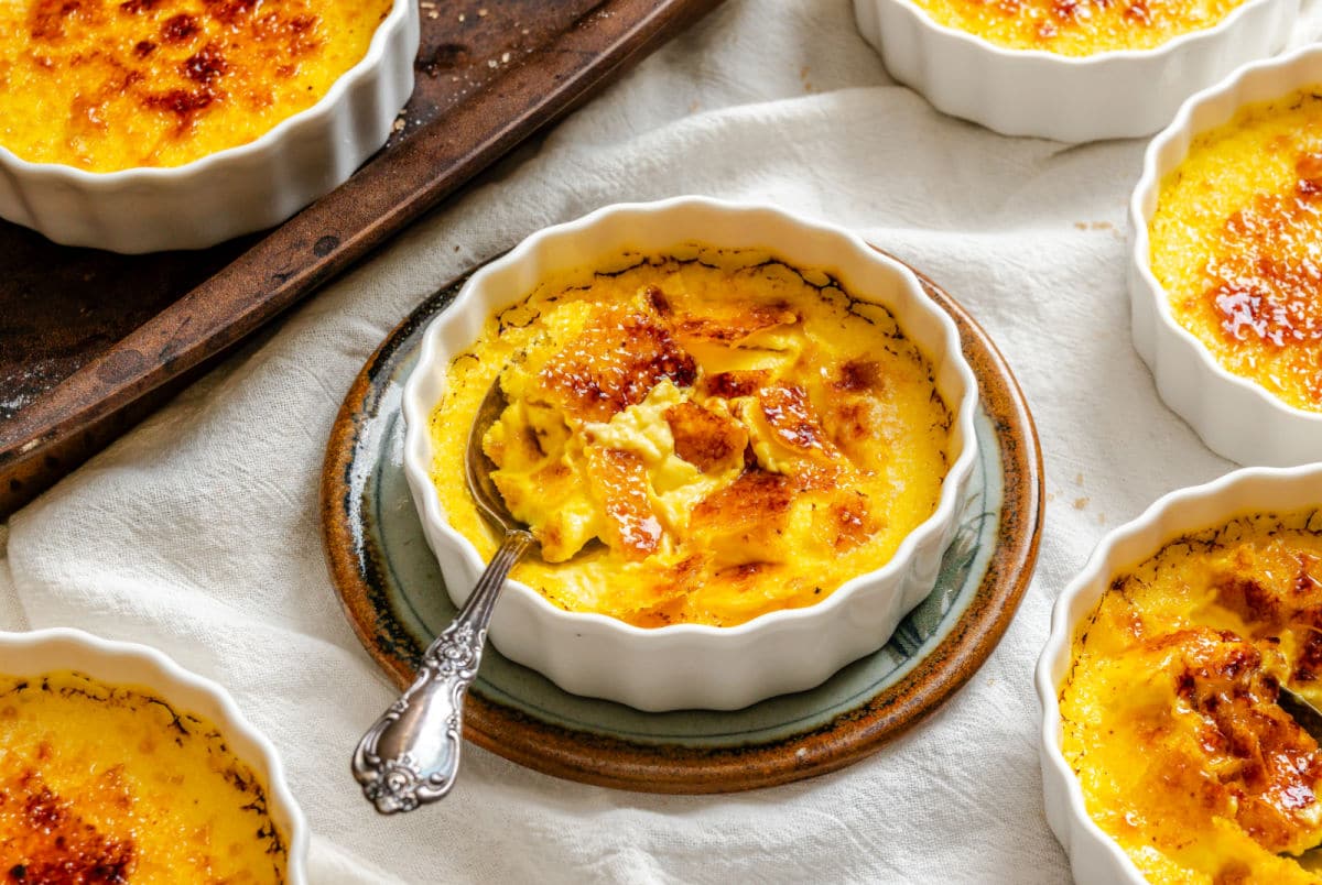 A ramekin of creme brulee next to the baking sheet with more ramekins on it.