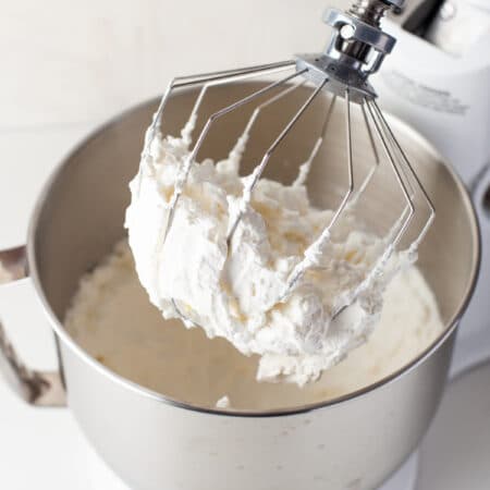 Homemade whipped cream on a whisk attachment of a stand mixer.