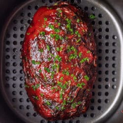 A meatloaf in an air fryer topped with sauce and parsley.