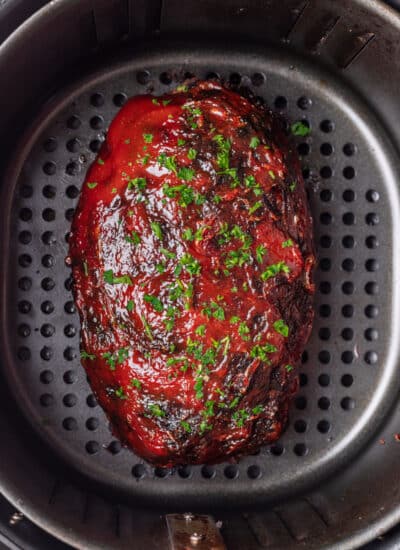 A meatloaf in an air fryer topped with sauce and parsley.