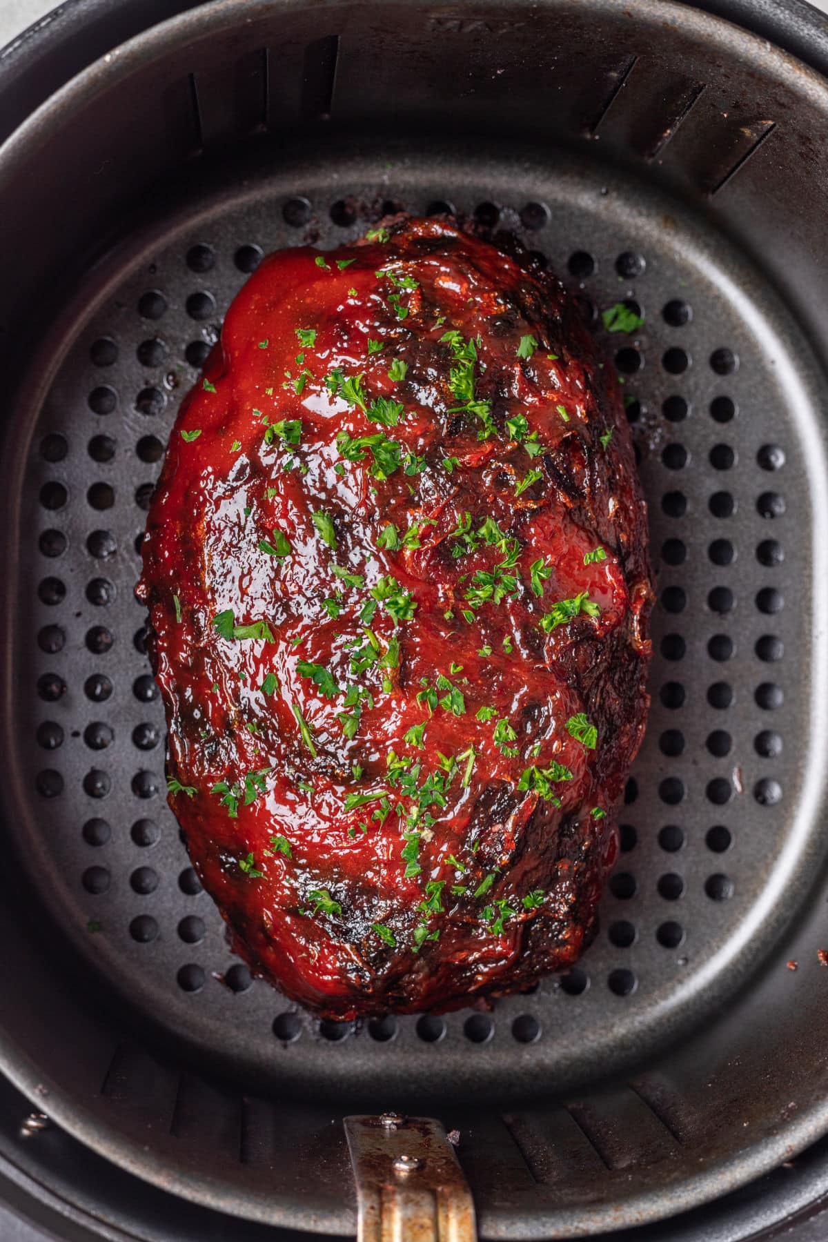 A meatloaf in an air fryer topped with sauce and parsley.