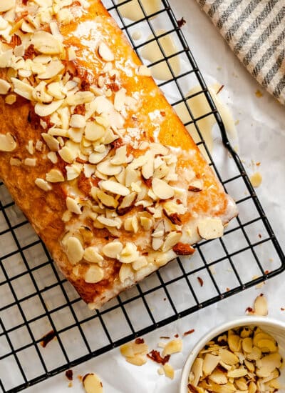 An unsliced loaf of almond quick bread next to a dish of sliced almonds.