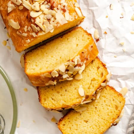 Three slices of almond quick bread next to the loaf.