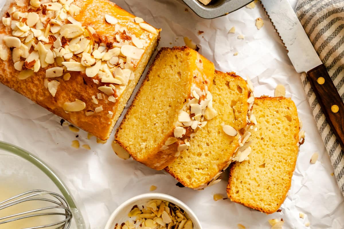 Slices of almond quick bread next to a knife and a bread pan.
