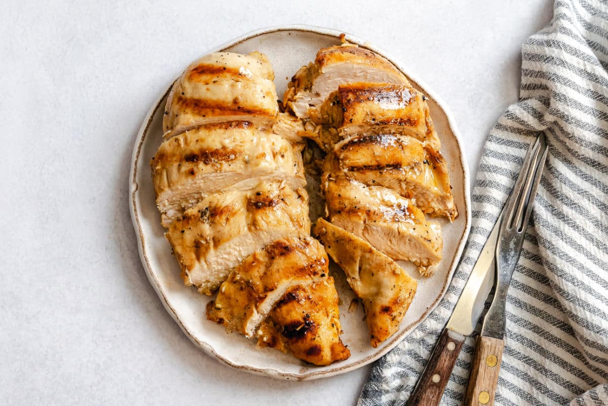 Two grilled Caesar marinated chicken breasts sliced on a plate. 