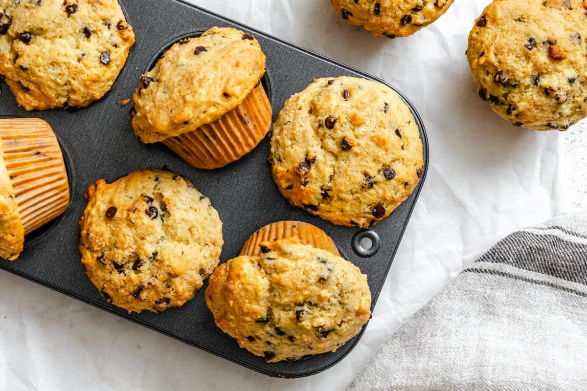 Bakery style chocolate chip muffins in a muffin tin at an angle.