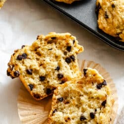A bakery style chocolate chip muffin in half on a paper liner.