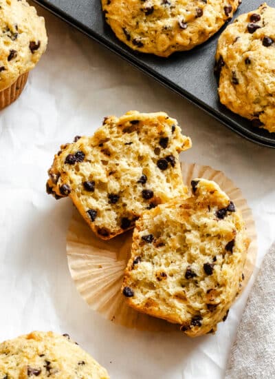 A bakery style chocolate chip muffin in half on a paper liner.