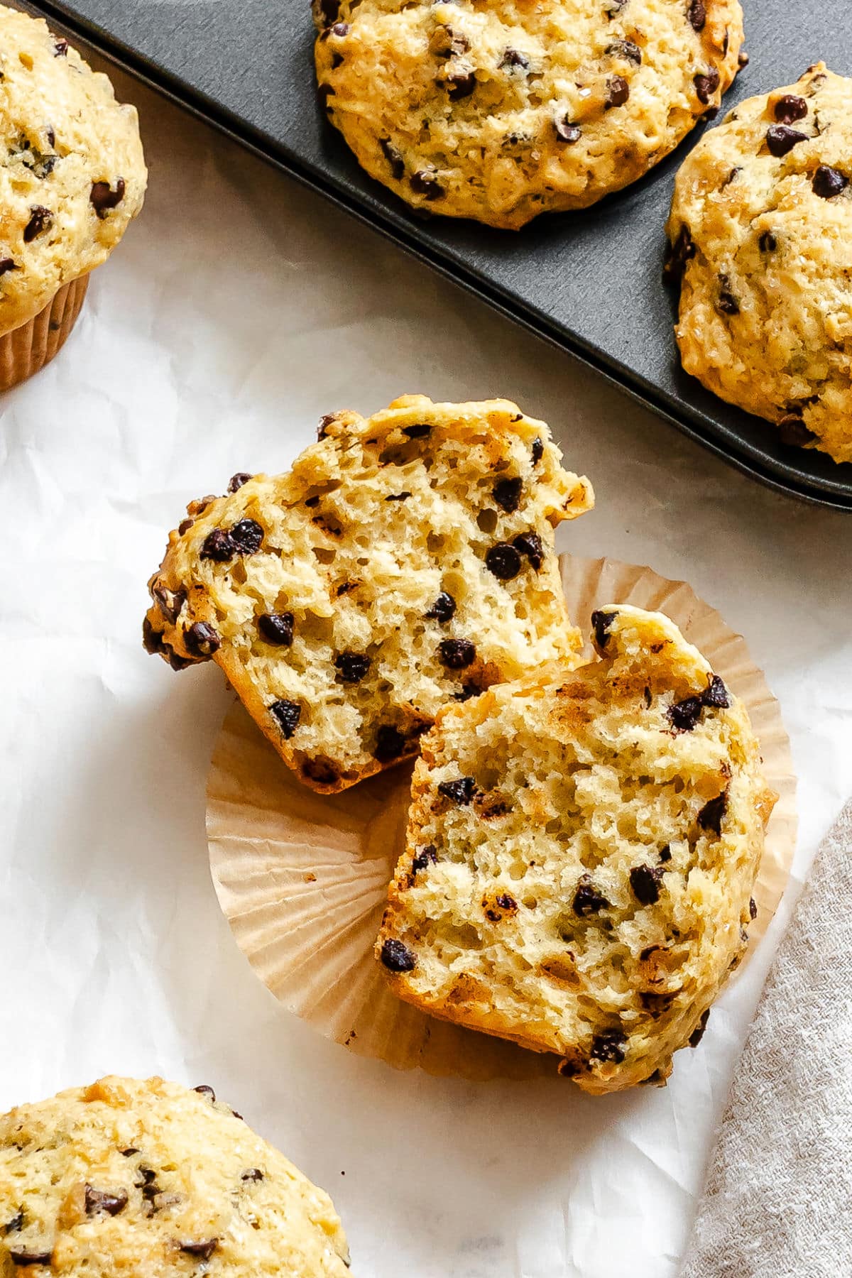A bakery style chocolate chip muffin in half on a paper liner.