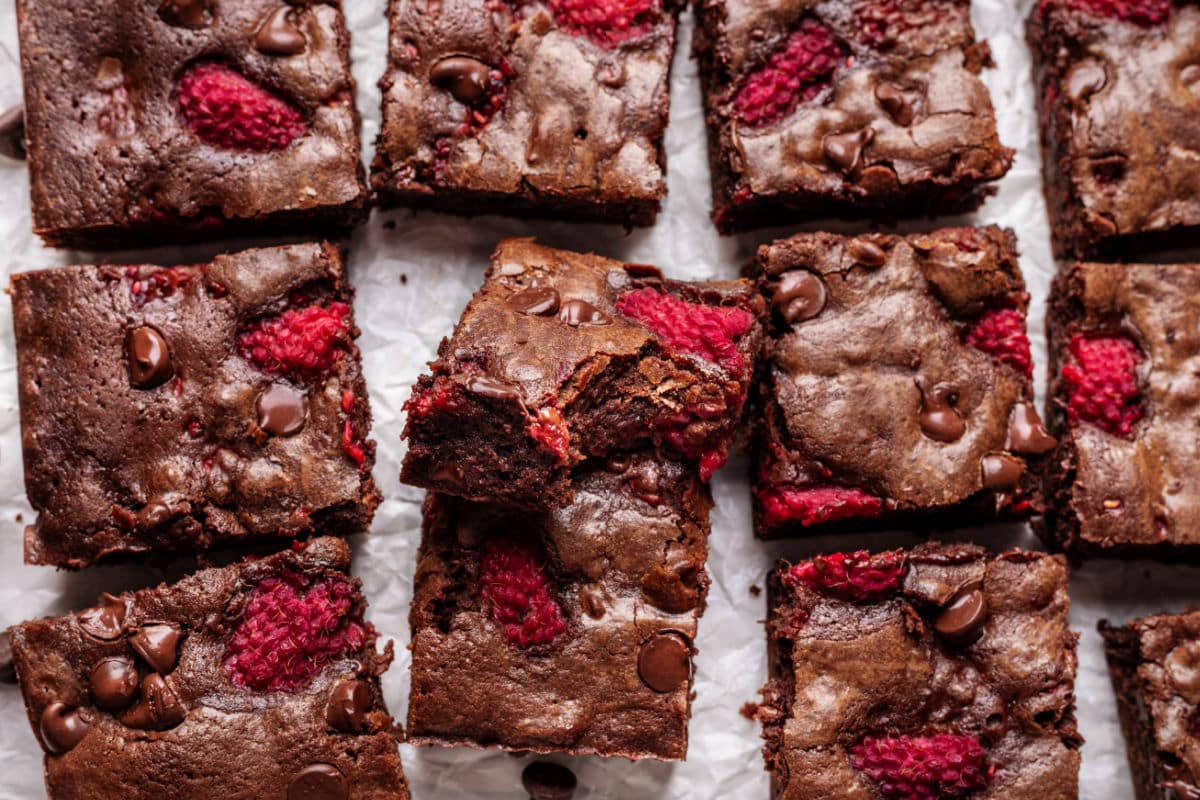 Chocolate raspberry brownies cut next to each other, one with a bite missing.