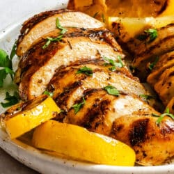 Sliced grilled Green chicken next to lemon slices.