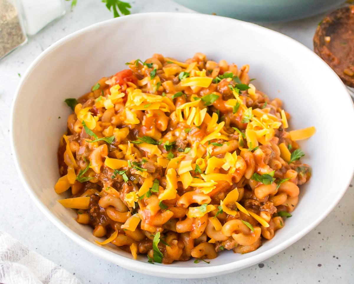 Homemade Hamburger Helper A white bowl of homemade Hamburger helper topped with shredded cheese.