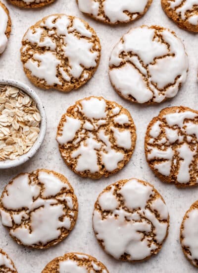 Iced oatmeal cookies next to a dish of oats.