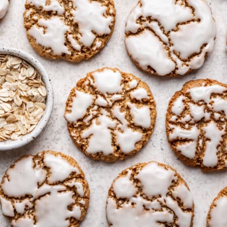 Iced oatmeal cookies next to a dish of oats.