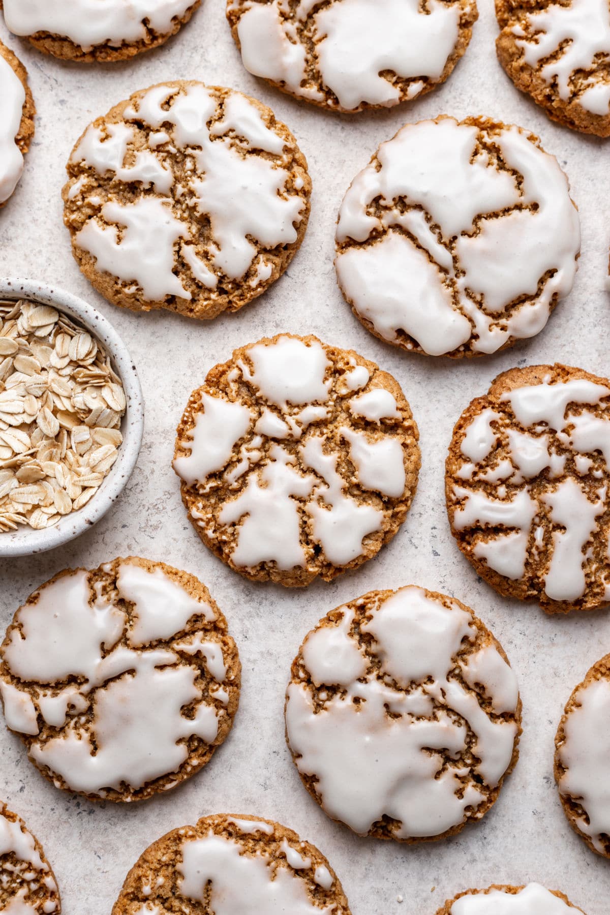 Iced oatmeal cookies next to a dish of oats.