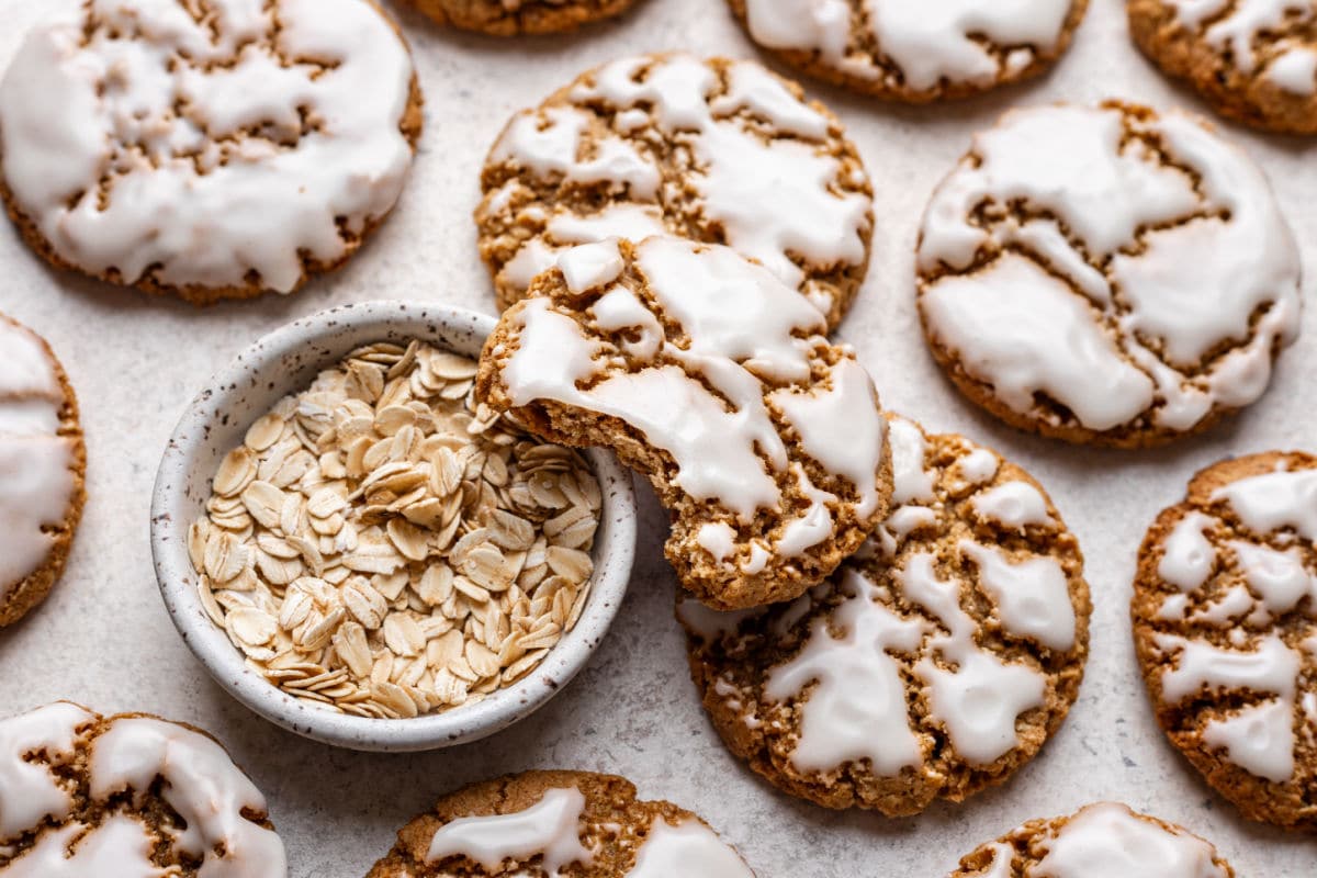 An iced oatmeal cookie with a bite missing leaning against a dish of oats.
