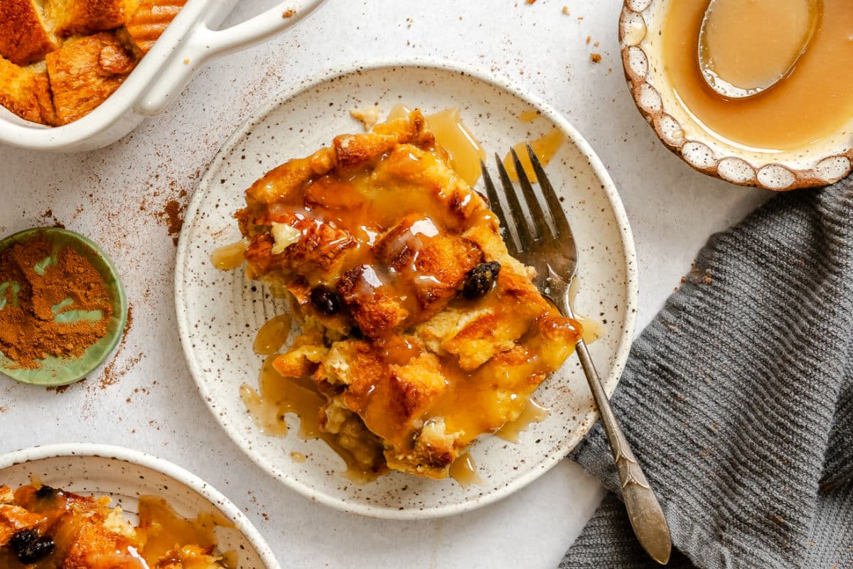 A piece of Irish bread pudding topped with sauce on a plate with a fork.