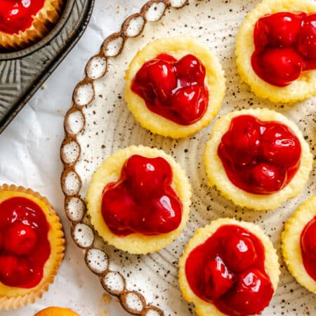 A platter of mini cherry cheesecakes next to the muffin tin.