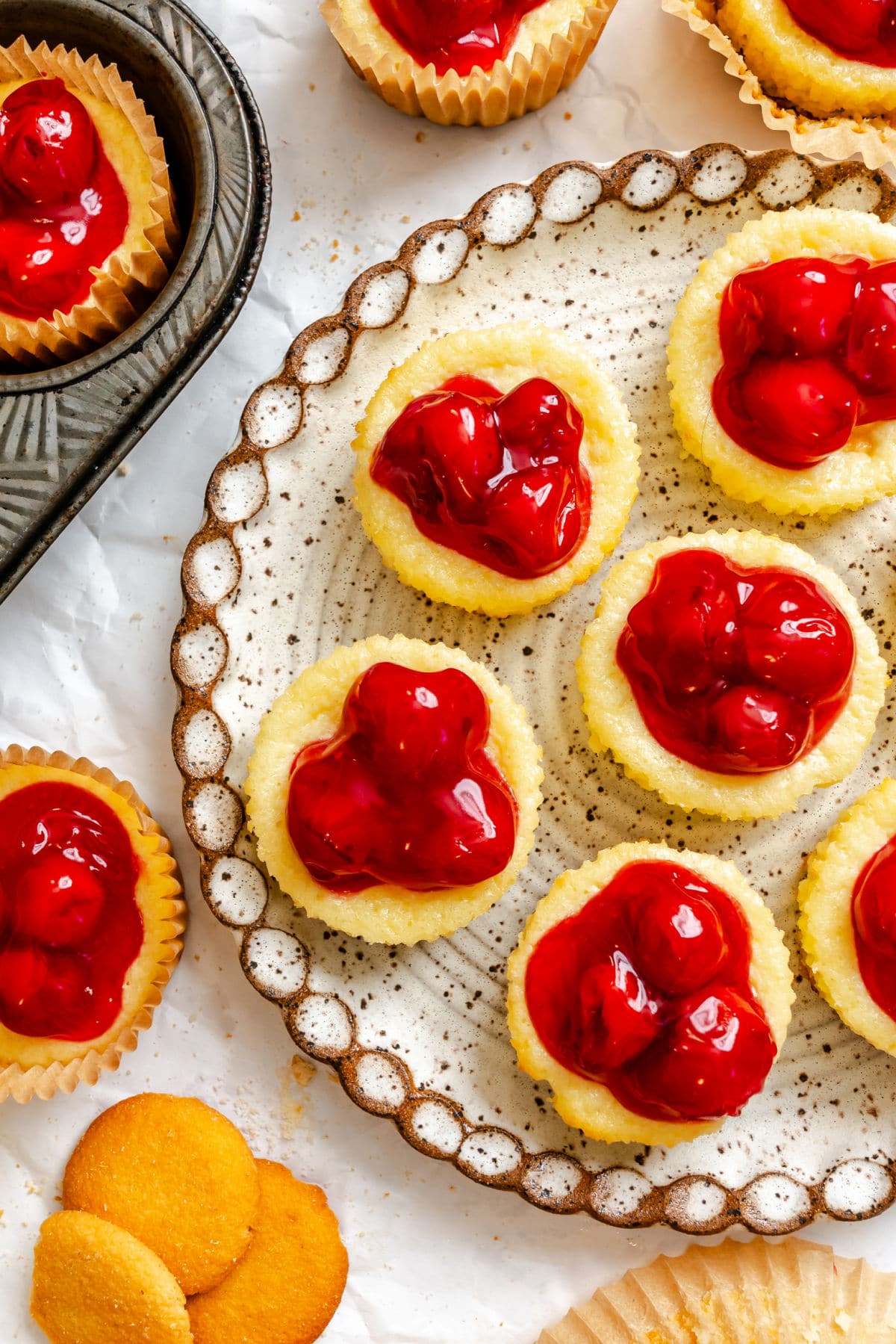 A platter of mini cherry cheesecakes next to the muffin tin.