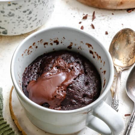 A chocolate lava molten cake in a mug next to pieces of baking chocolate.