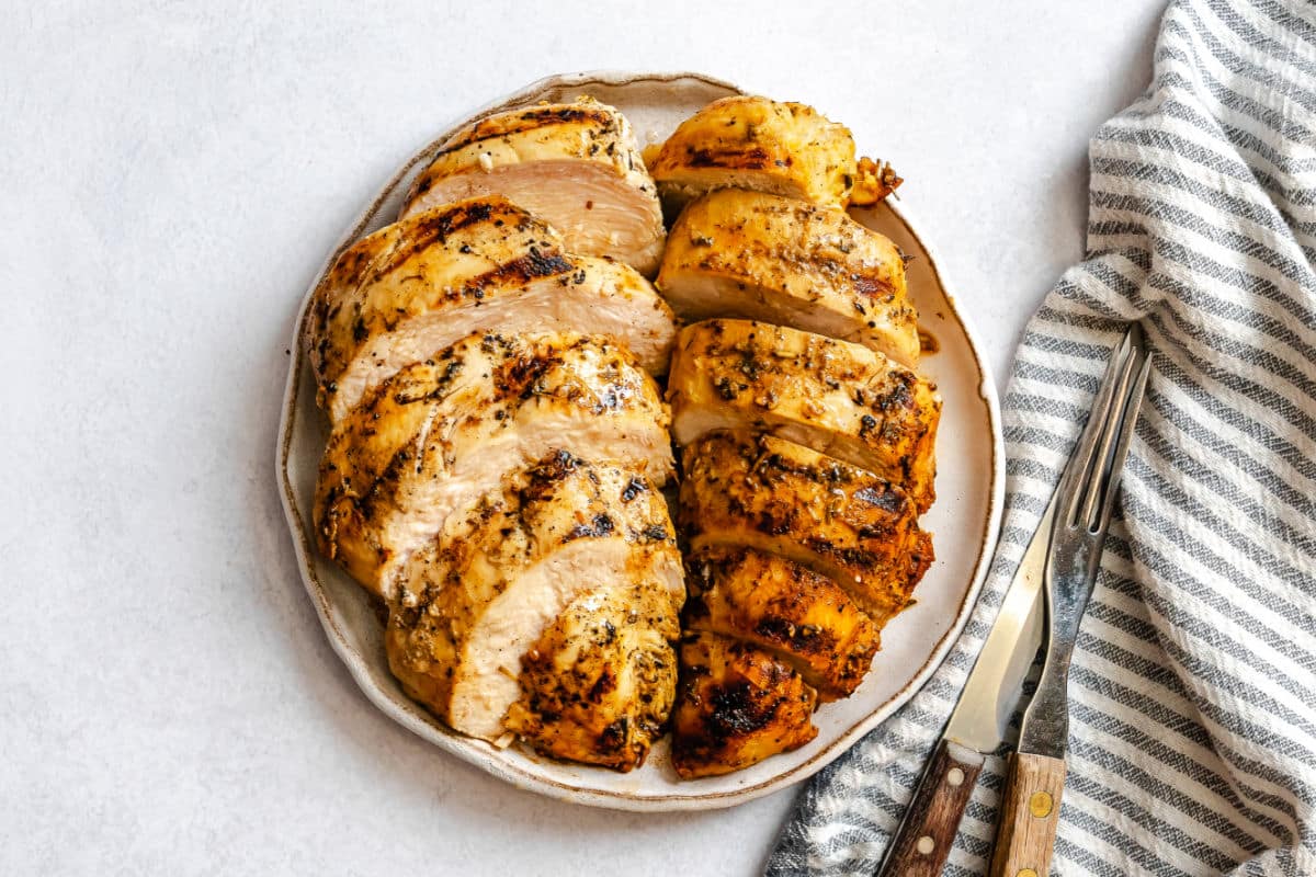 Une assiette avec deux poitrines de poulet marinées aux herbes et à la moutarde grillées et tranchées.