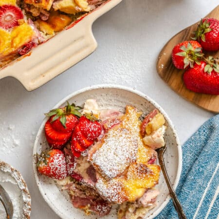 A plate of strawberry cream cheese French toast casserole topped with fresh strawberries and powdered sugar.