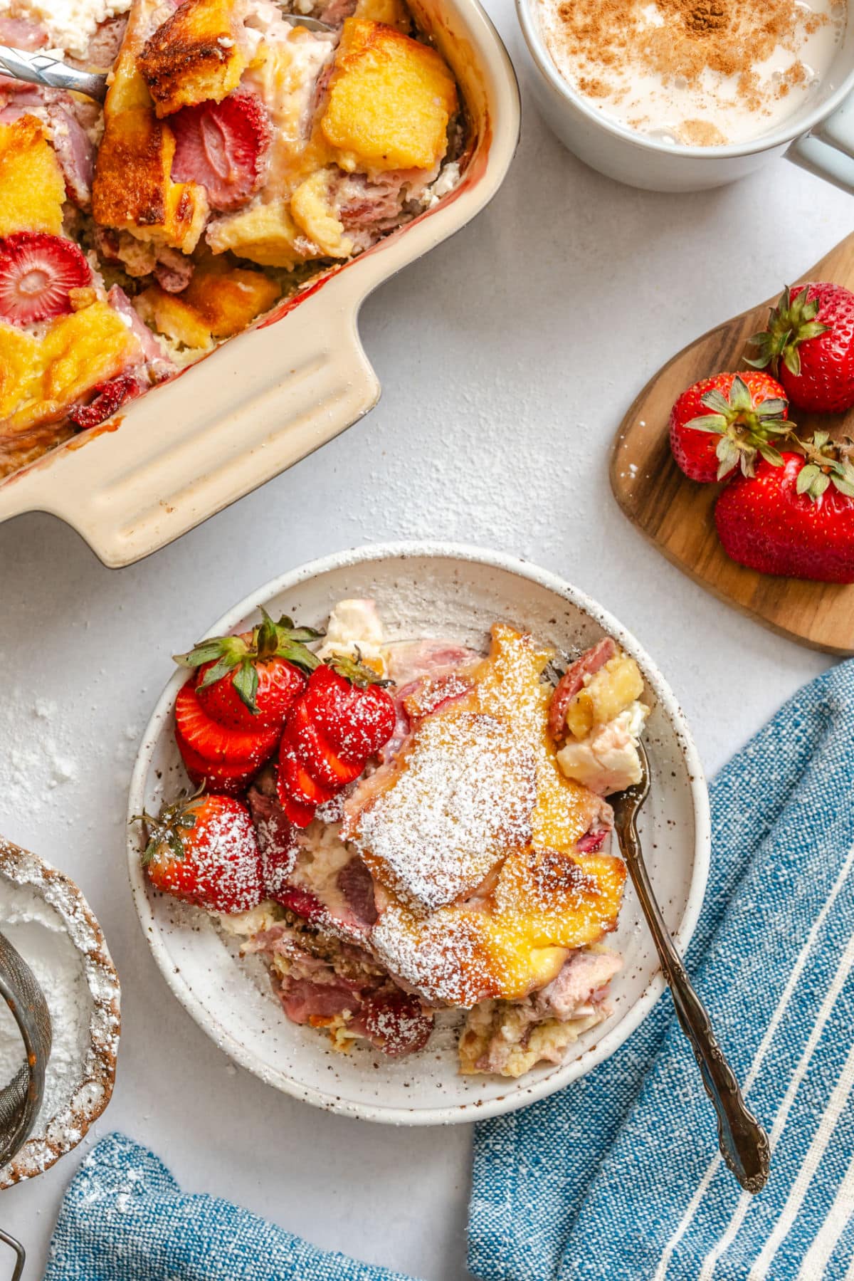 A plate of strawberry cream cheese French toast casserole topped with fresh strawberries and powdered sugar.
