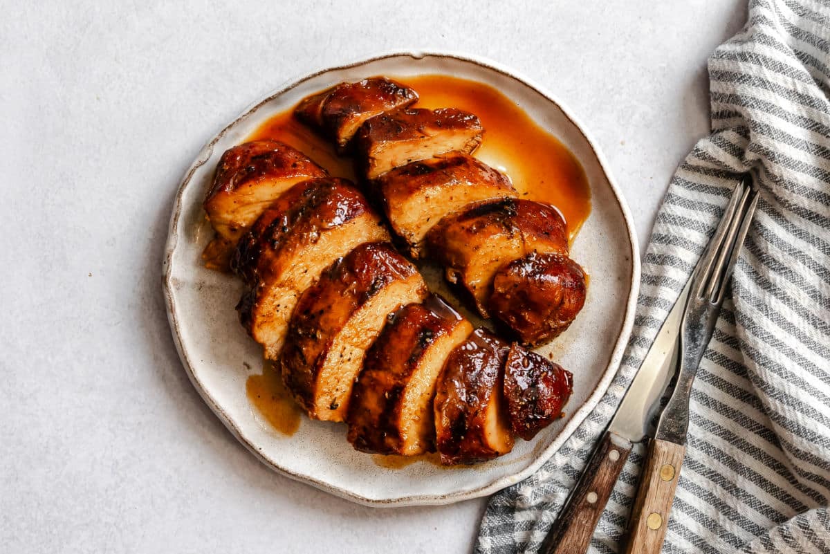Une assiette avec deux poitrines de poulet teriyaki marinées et grillées tranchées.