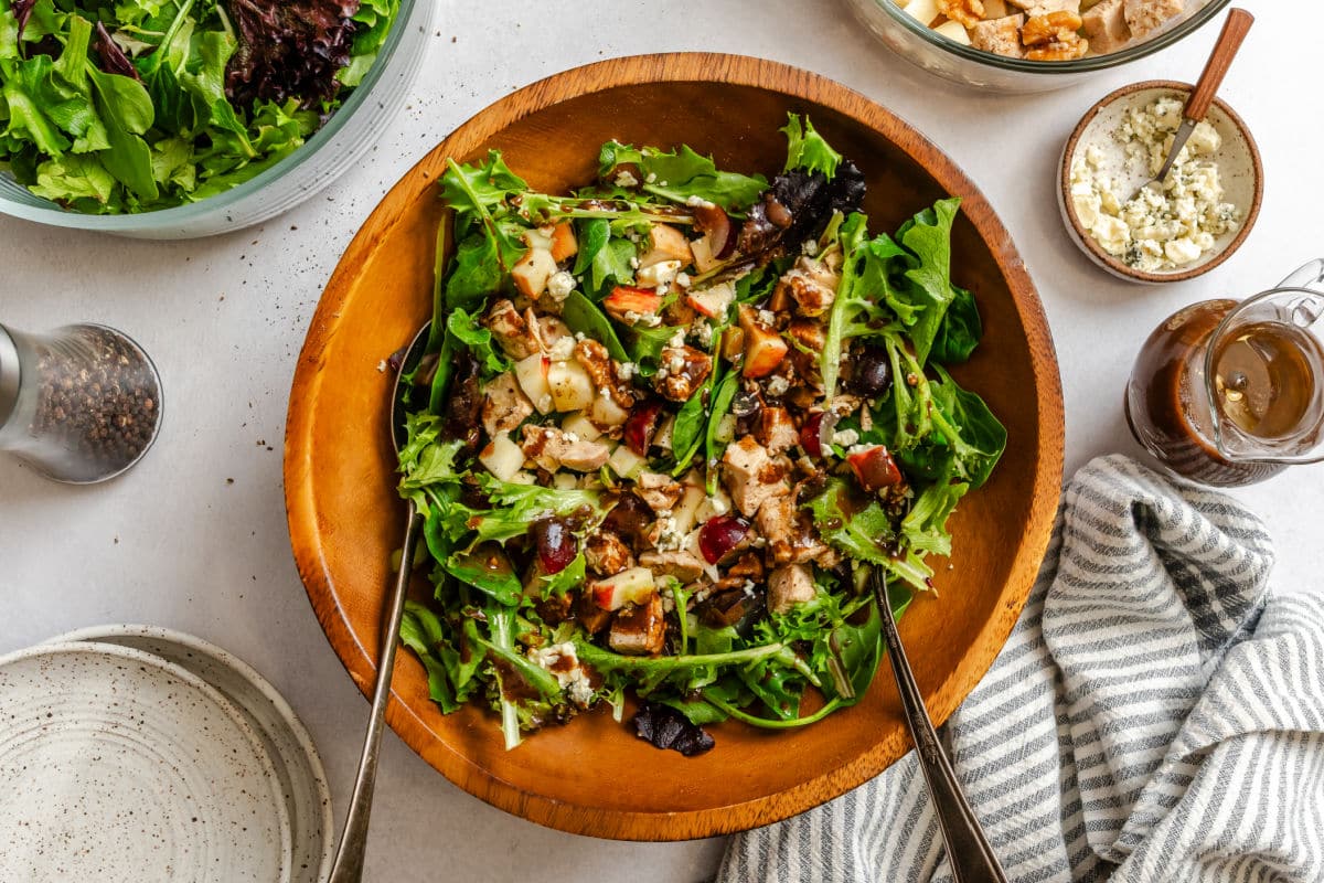 Waldorf Salad California Pizza Kitchen Copycat Waldorf salad in a wooden bowl next to a vial of dressing and toppings.