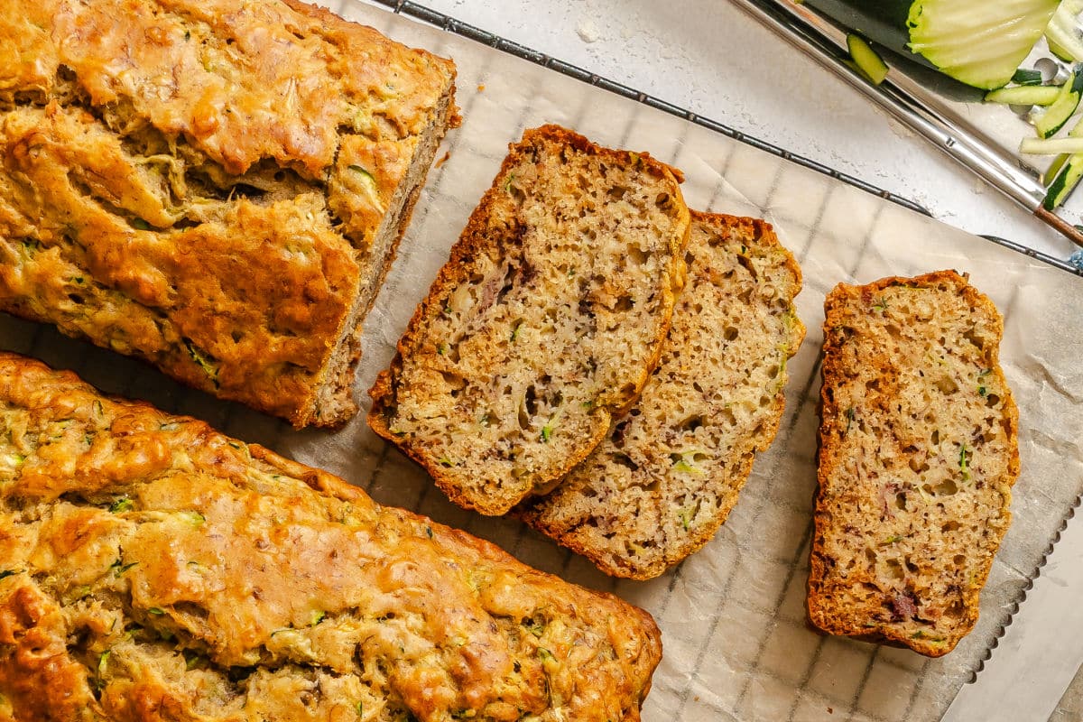 A partially sliced loaf of zucchini banana bread on a wire cooling rack.