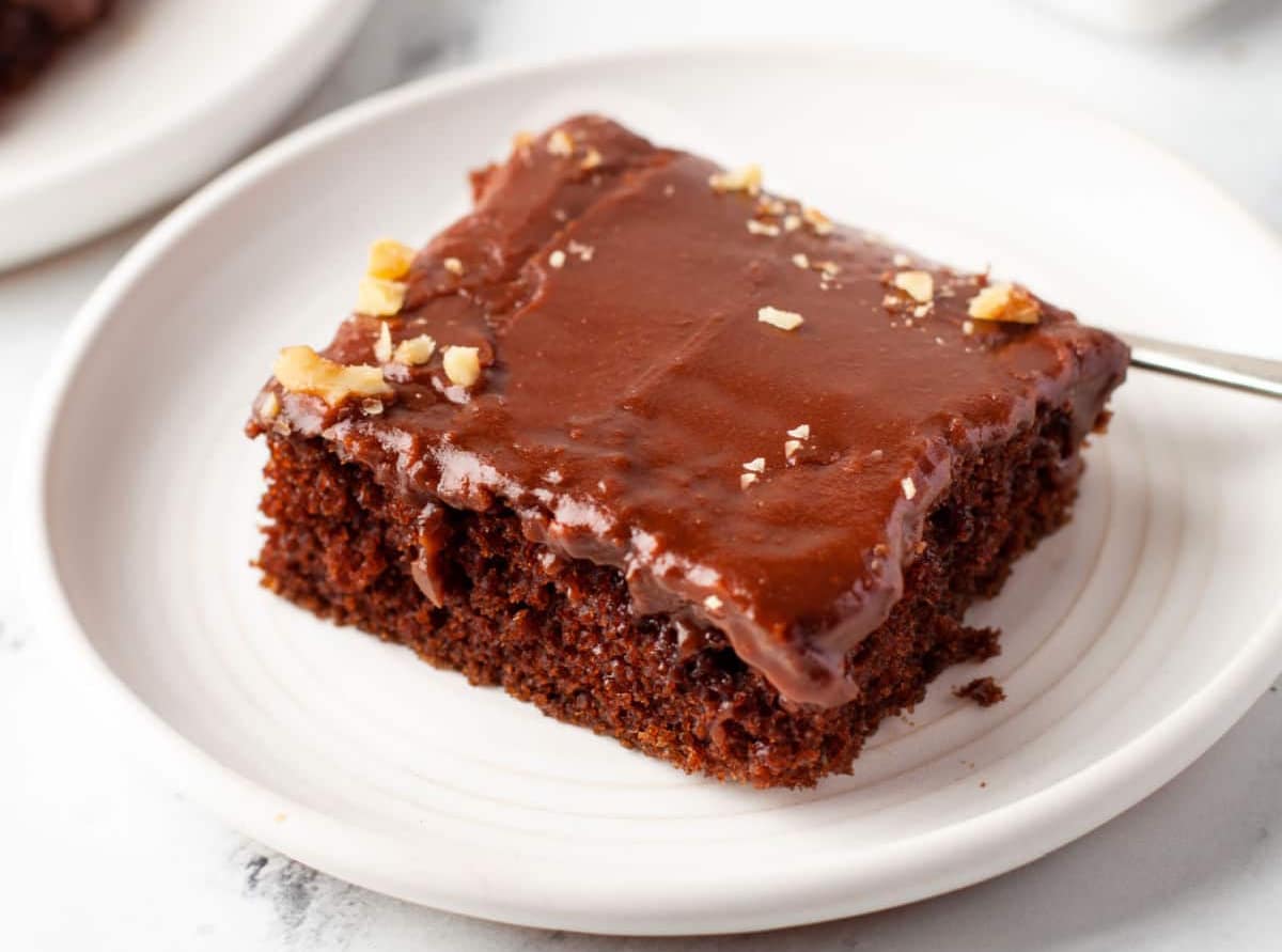 A slice of Texas sheet cake on a white plate next to another slice on a white plate.
