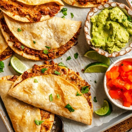 Crispy baked tacos on a baking sheet with dishes of chopped tomatoes and guacamole.