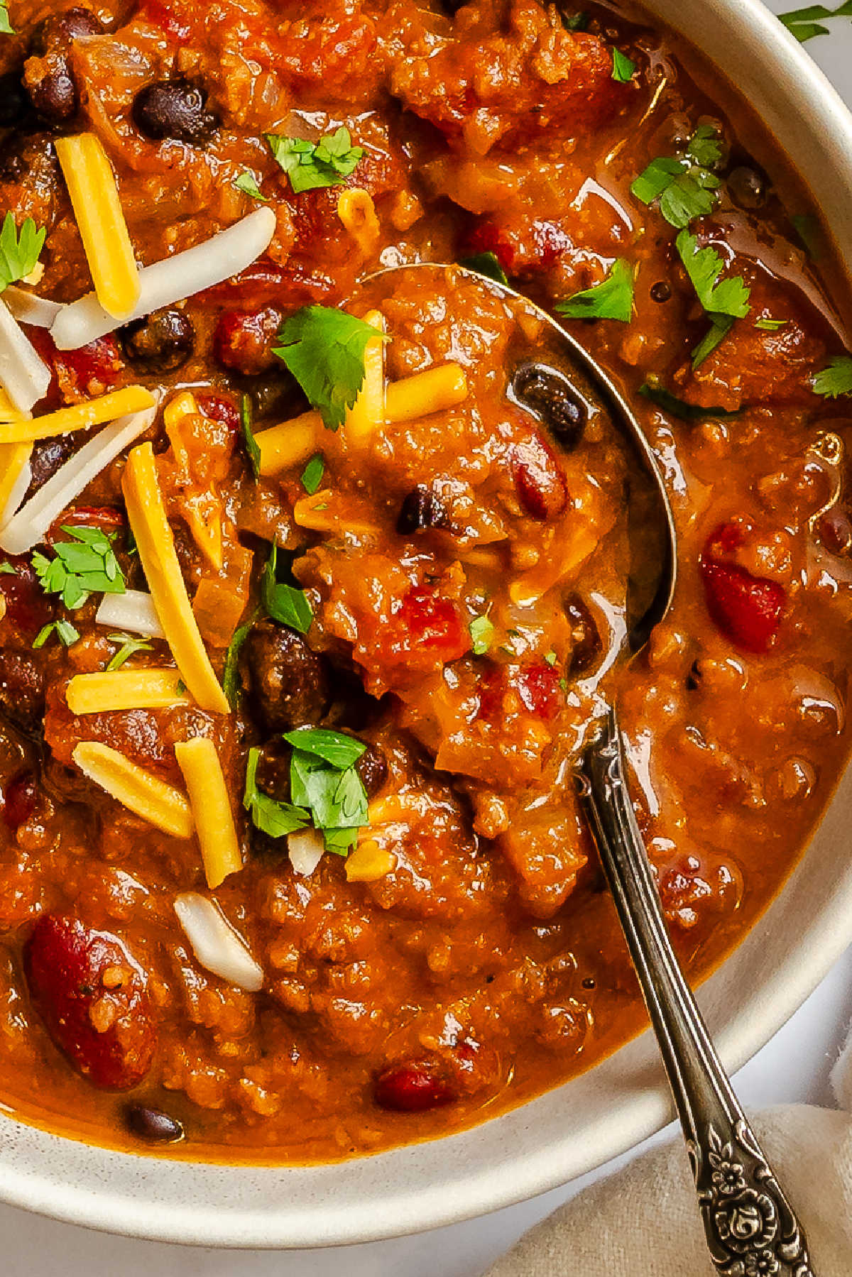 Close up of a bowl of barbecue chili with a silver spoon in it. 