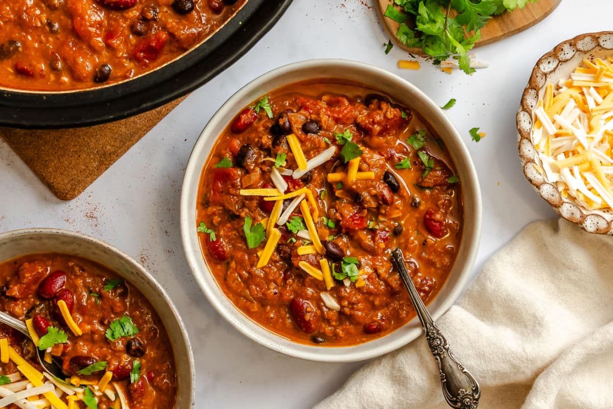 Two bowls of barbecue chili next to a pot of chili.