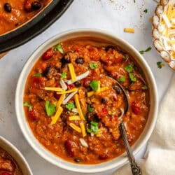 A bowl of barbecue chili topped with sliced green onions and shredded cheese.