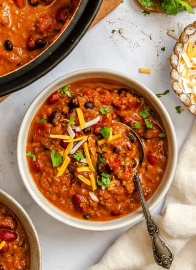 A bowl of barbecue chili topped with sliced green onions and shredded cheese.