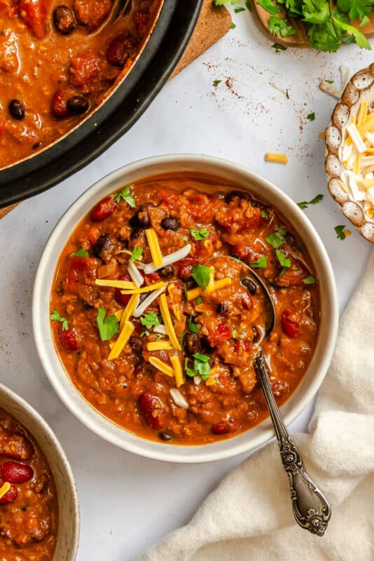 A bowl of barbecue chili topped with sliced green onions and shredded cheese.