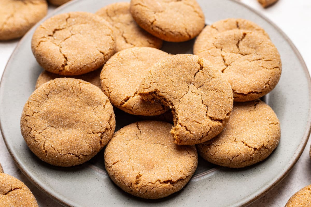 A cookie with a bite missing on top of a plate of brown sugar cookies.