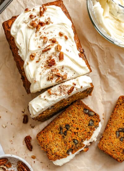 A partially sliced loaf of carrot loaf cake next to a bowl of cream cheese frosting.