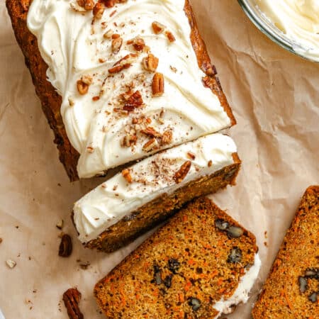 A partially sliced loaf of carrot loaf cake next to a bowl of cream cheese frosting.