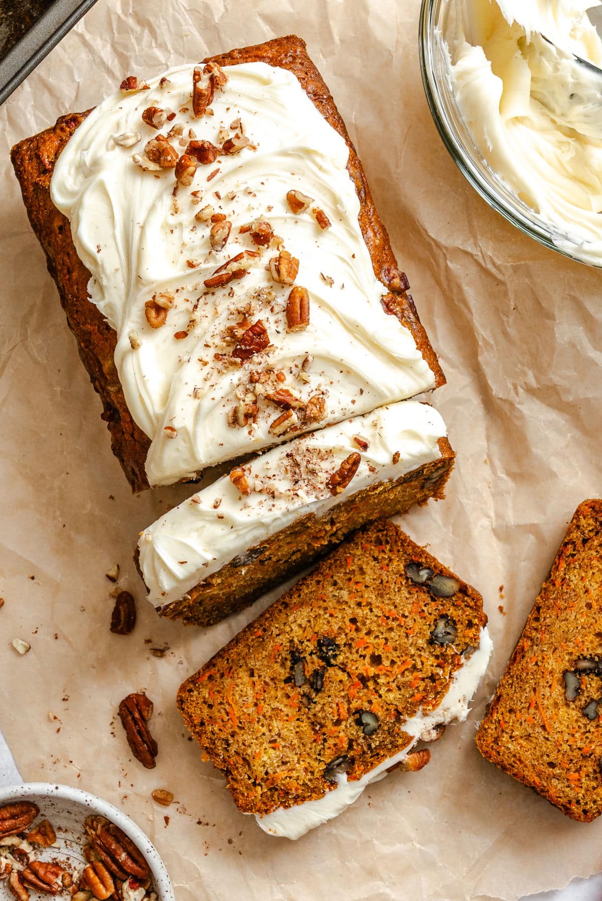 A partially sliced loaf of carrot loaf cake next to a bowl of cream cheese frosting.