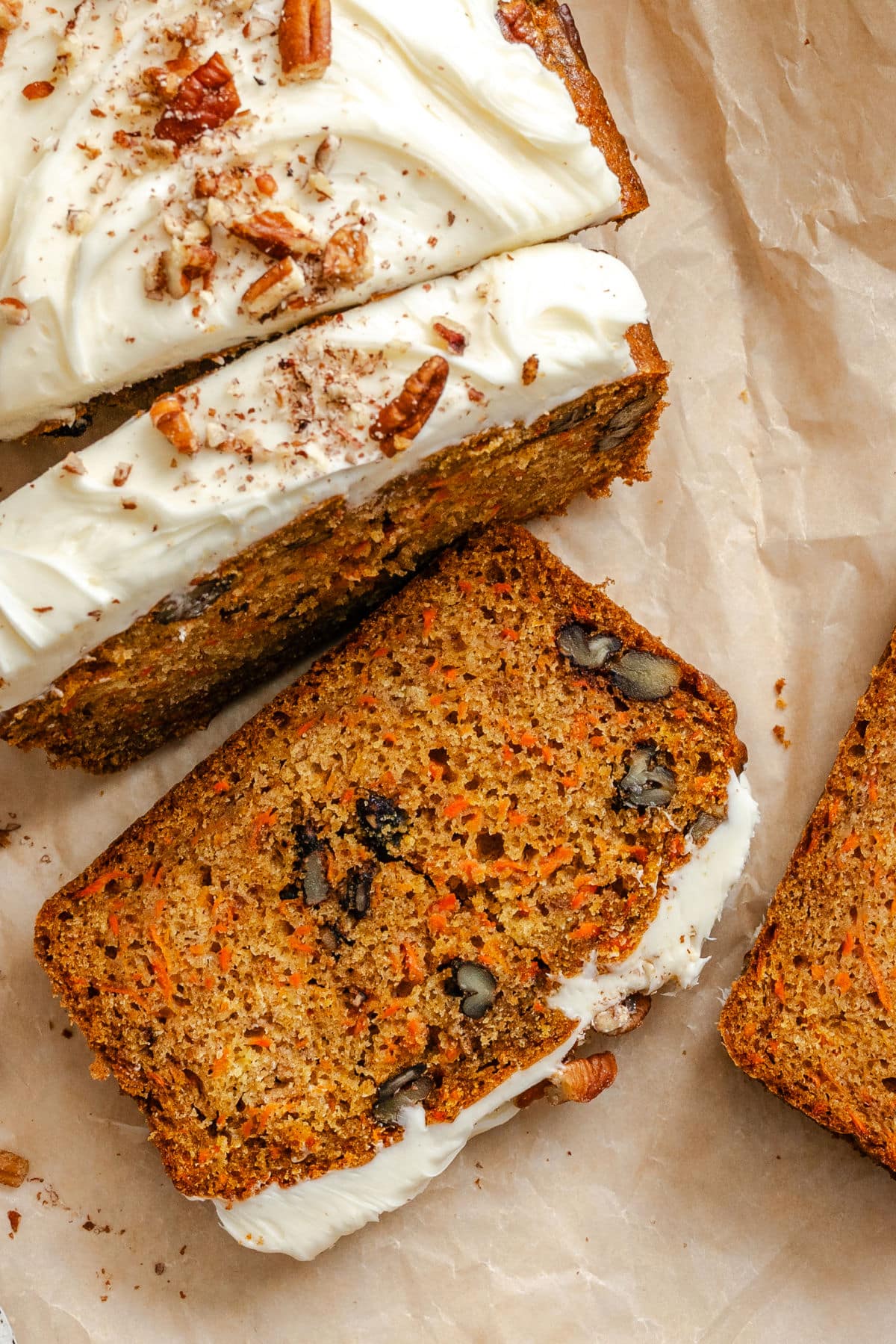 Slices of carrot loaf cake topped with cream cheese frosting and chopped pecans.
