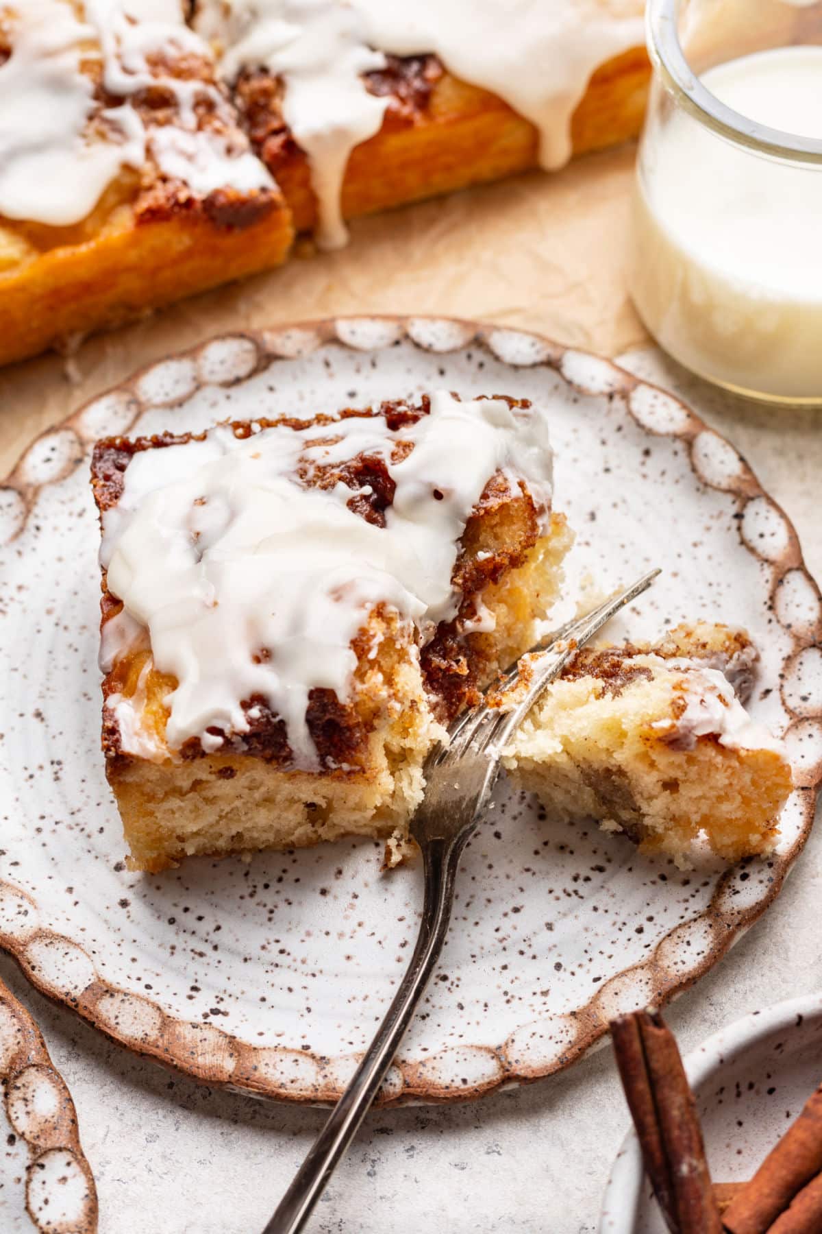 A piece of cinnamon roll cake on a plate with a fork taking a bite. 
