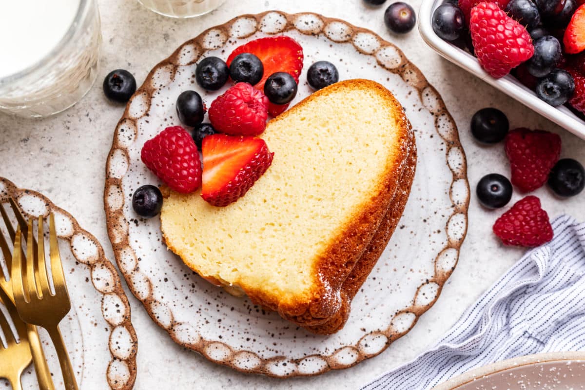 A slice of cream cheese pound cake with fresh berries on the plate. 